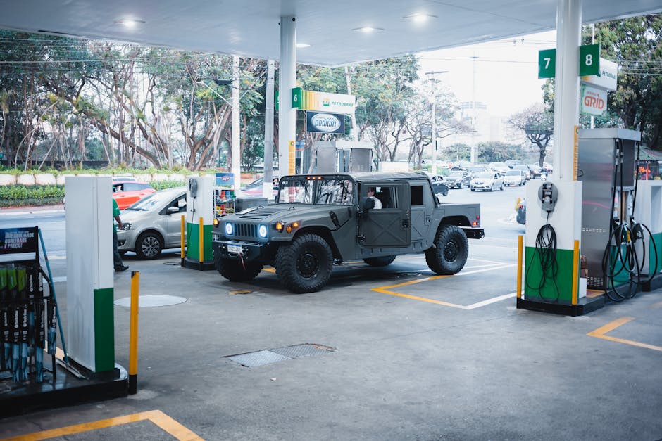 A white off-road vehicle with a rugged, textured exterior and large, knobby tires is parked directly in front of a grey single-story garage with a pitched roof. The vehicle's front, featuring a distin